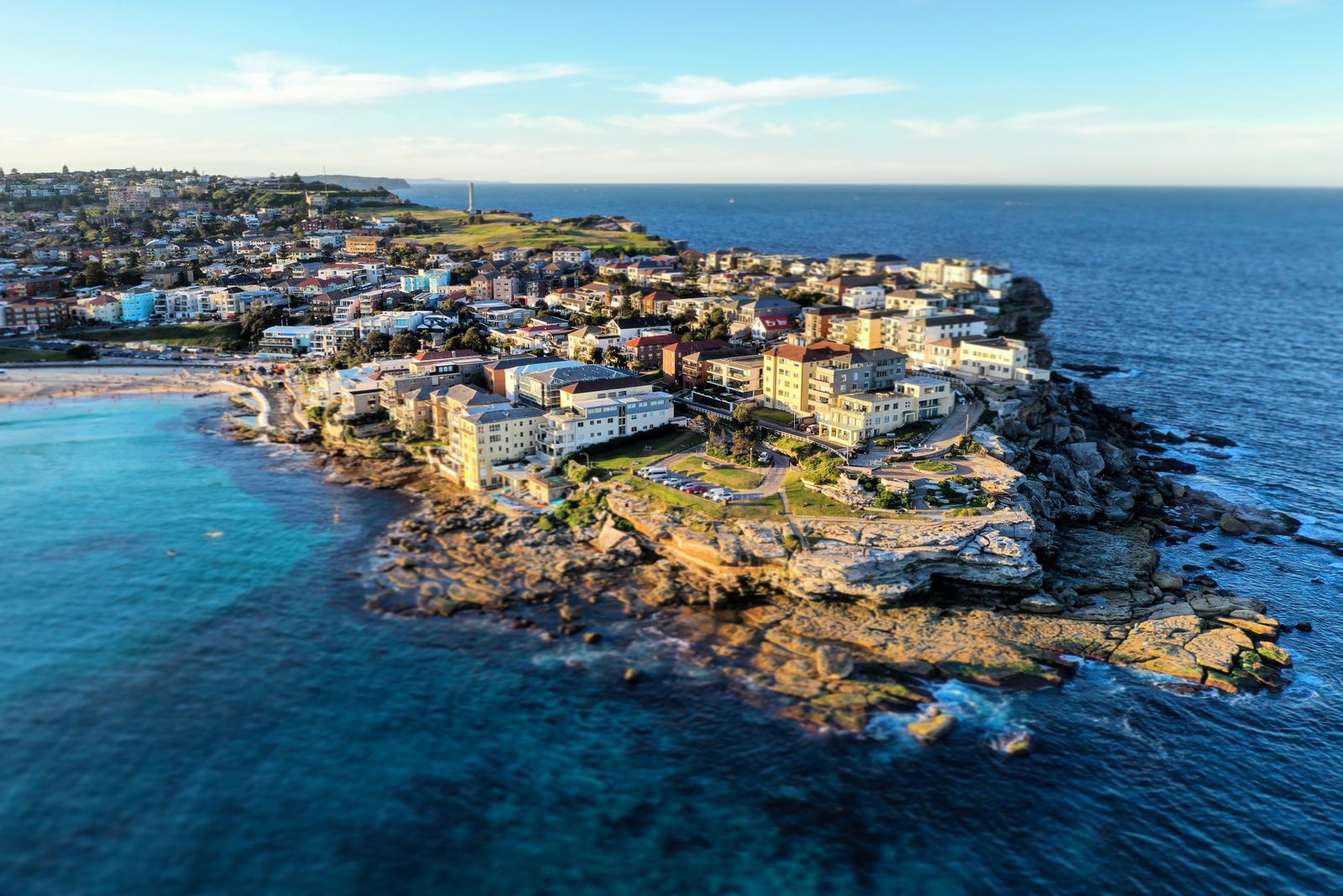 Aerial view of the Bondi headland, turquoise water wrapping around sandstone cliffs and a tight grid of beachside houses.