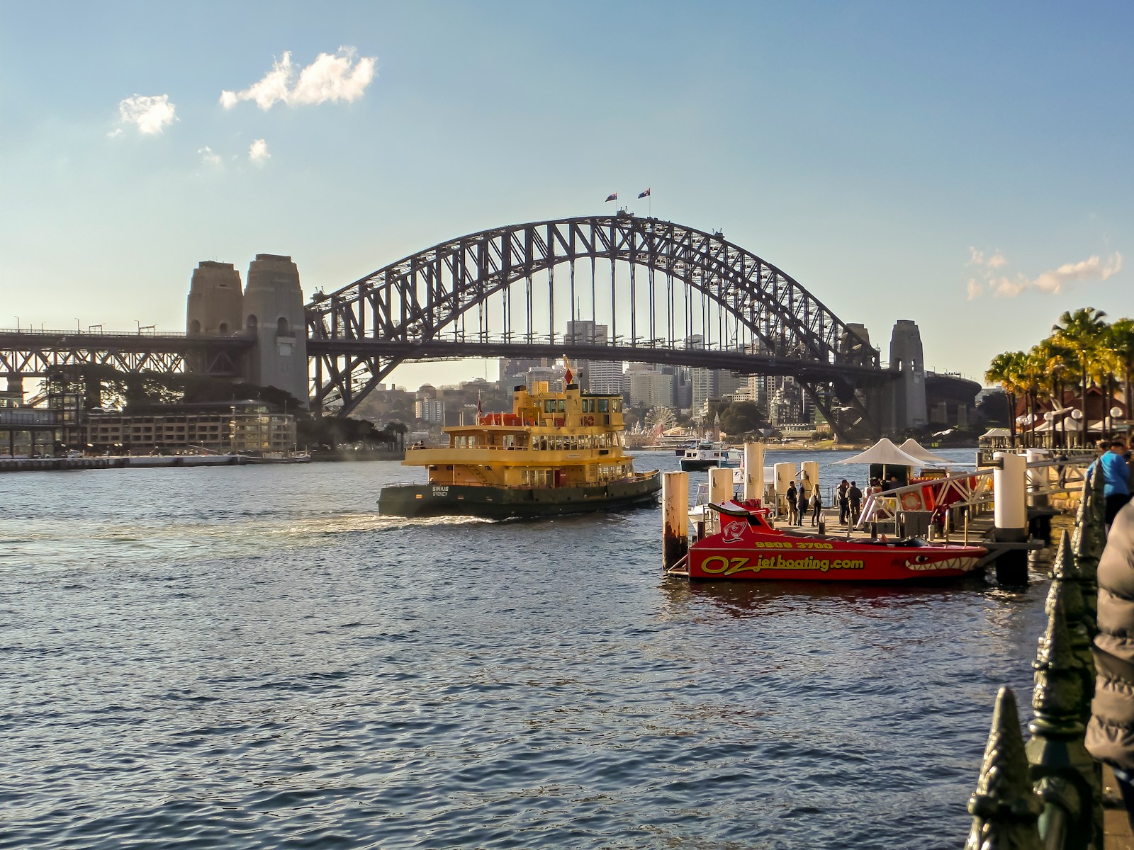 A yellow Sydney ferry crossing the harbour beneath the steel arch of the Harbour Bridge on a bright afternoon.